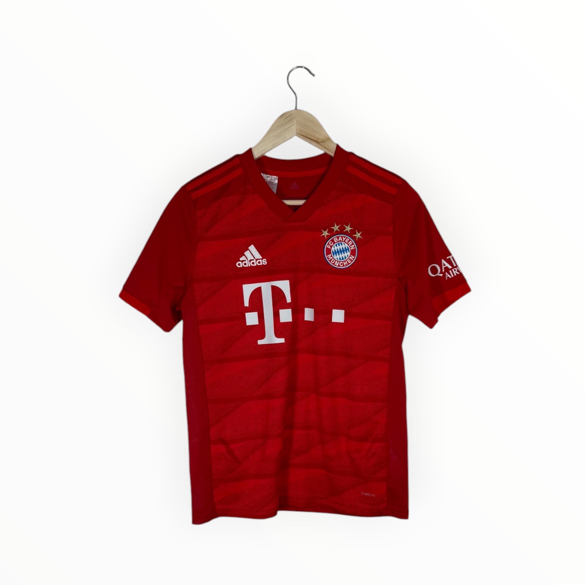 A red Adidas Bayern Munich soccer jersey hanging on a wooden hanger against a plain white background. The jersey features the white Adidas logo on the right chest, the Bayern Munich club crest on the left chest, and the large white T-Mobile sponsor logo across the center.