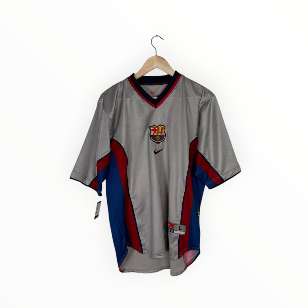 A vintage FC Barcelona short-sleeve soccer jersey in gray, featuring red and blue side panels, hanging on a wooden hanger against a white background.