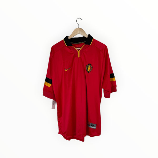 A red Belgium national football team jersey by Nike, featuring a black and gold collar, black and gold sleeve stripes, and the Belgian crest on the chest, hanging on a wooden hanger against a white background.