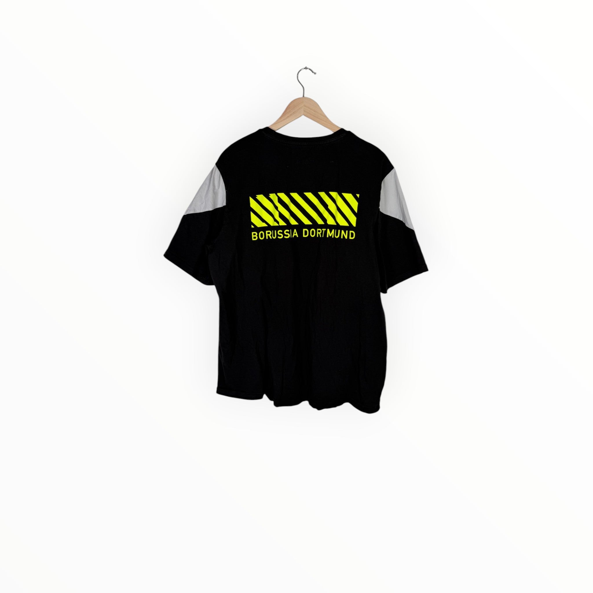A black short-sleeve t-shirt with gray sleeve panels and a yellow high-visibility hazard stripe graphic on the chest, hanging on a wooden hanger against a plain white background.