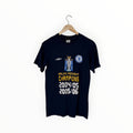 A navy blue Chelsea FC short-sleeve t-shirt hanging on a wooden hanger against a plain white background. The shirt features a graphic celebrating 2004/05 and 2005/06 Barclays Premiership Champions, with the Umbro logo on the right chest and the Chelsea crest on the left chest.