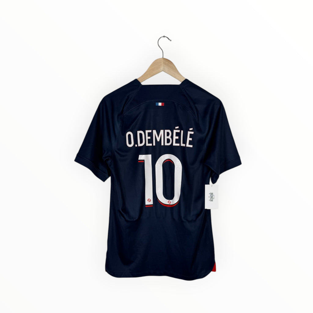 A navy blue soccer jersey with 'O. DEMBÉLÉ' and the number '10' printed on the back, hanging on a wooden hanger against a plain white background.