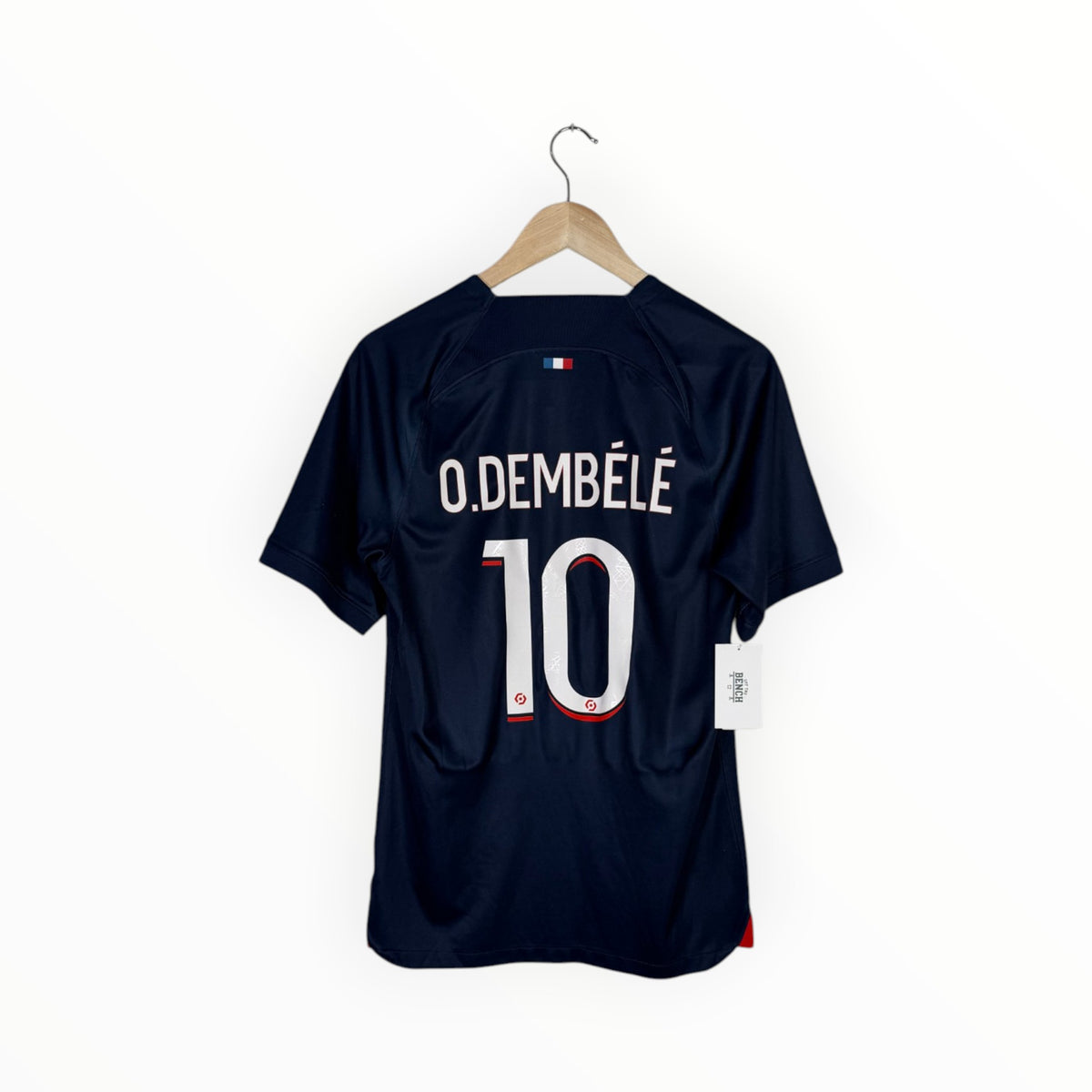 A navy blue soccer jersey with 'O. DEMBÉLÉ' and the number '10' printed on the back, hanging on a wooden hanger against a plain white background.