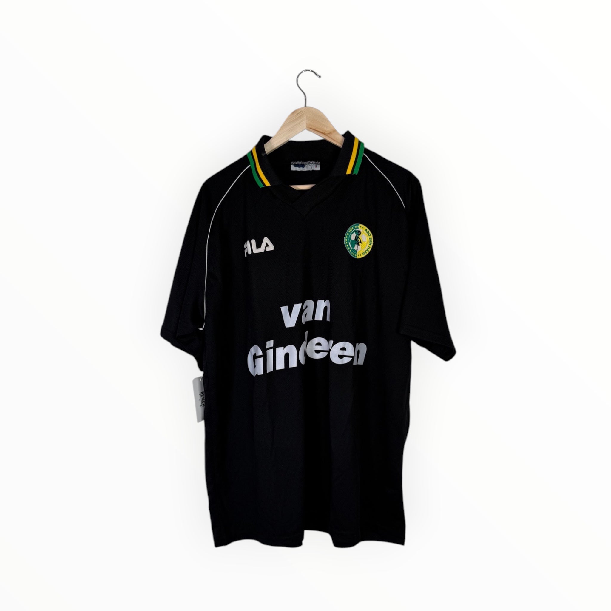 A vintage black Alva football jersey with 'van Gineen' sponsor text, hanging on a wooden hanger against a white background.