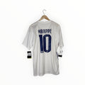 A white short-sleeve soccer jersey hanging on a wooden hanger against a plain white background. The back of the shirt features the name 'MBAPPE' and number '10' in dark blue.