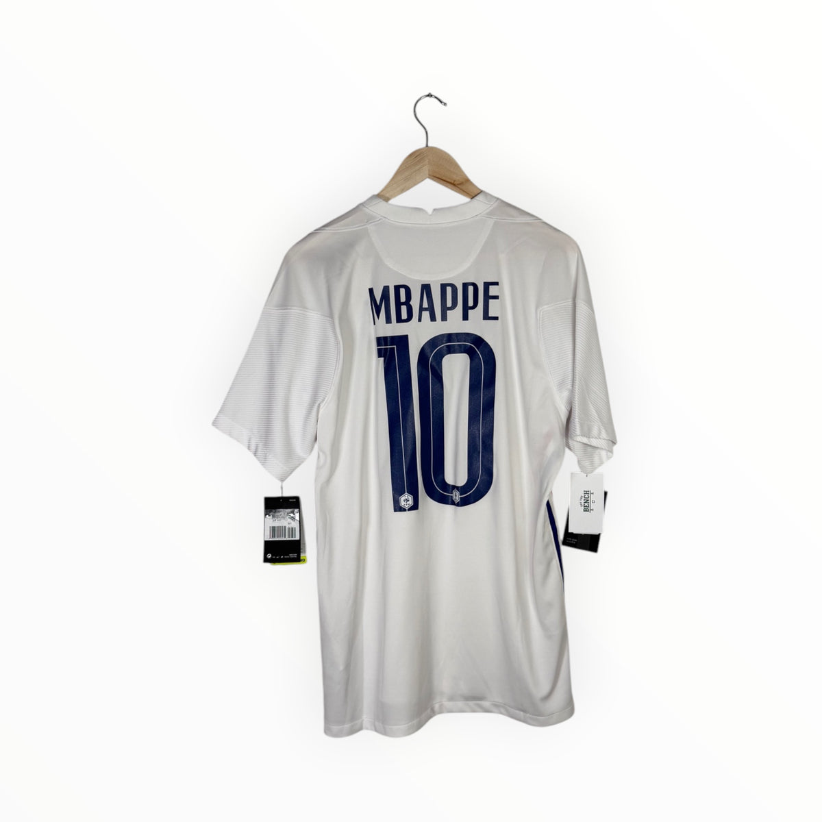 A white short-sleeve soccer jersey hanging on a wooden hanger against a plain white background. The back of the shirt features the name 'MBAPPE' and number '10' in dark blue.