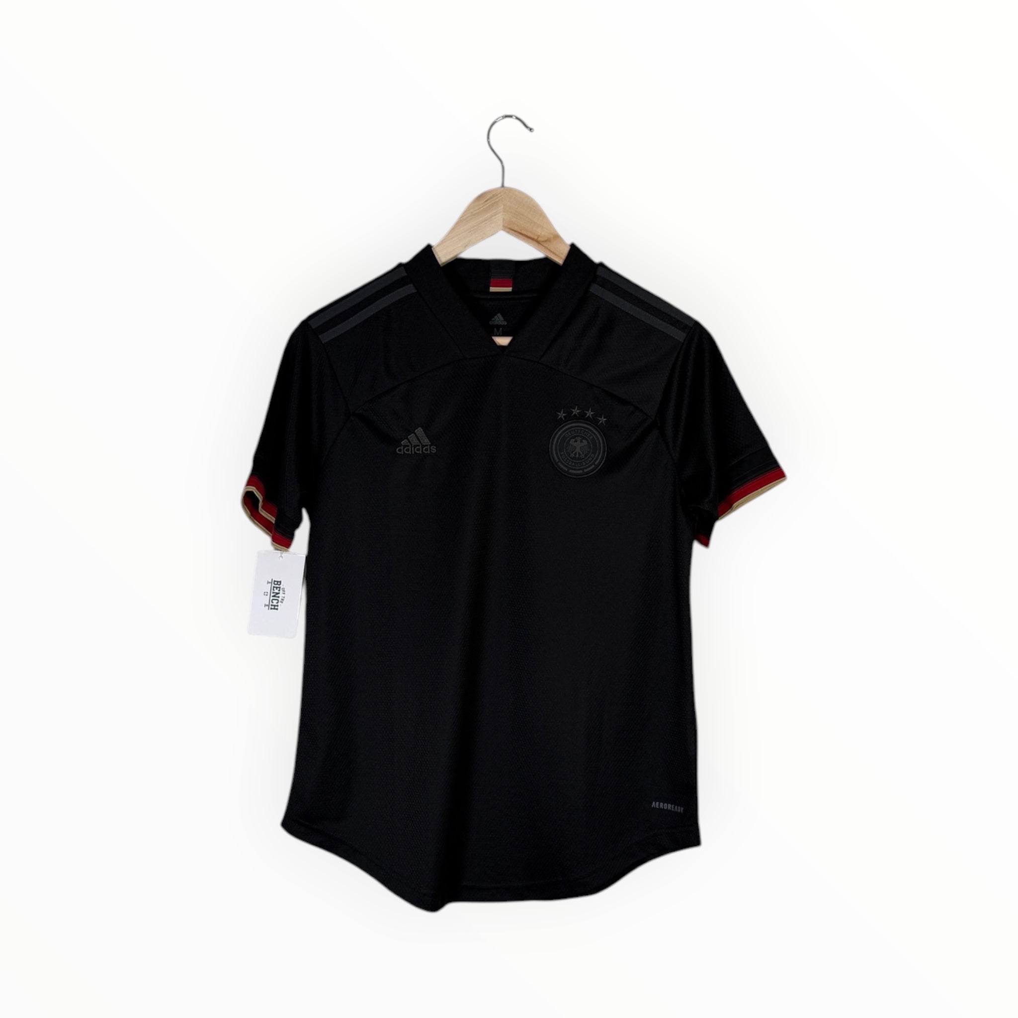 A black Adidas Germany soccer jersey hanging on a wooden hanger against a plain white background. The jersey features the German national team crest on the left chest, the Adidas logo on the right chest, and subtle red and gold trim on the sleeve cuffs.