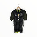 A Germany national football team home jersey with dark gray and black horizontal stripes, olive green sleeves, white Adidas branding and number 6, hanging on a wooden hanger against a white background.