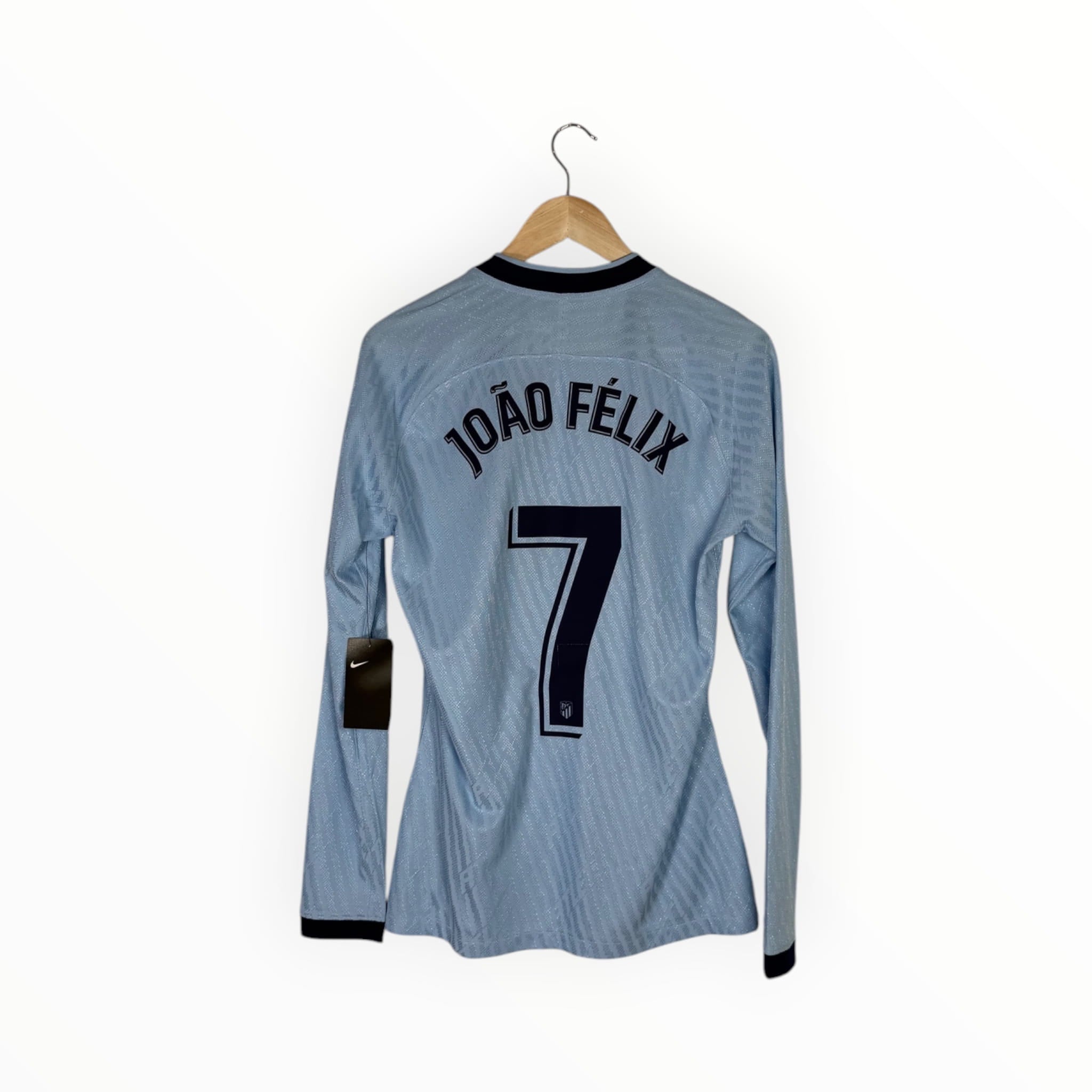 A light blue long-sleeve soccer jersey hanging on a wooden hanger against a white background, showing the back with 'JOÃO FÉLIX' and the number 7 printed in black.