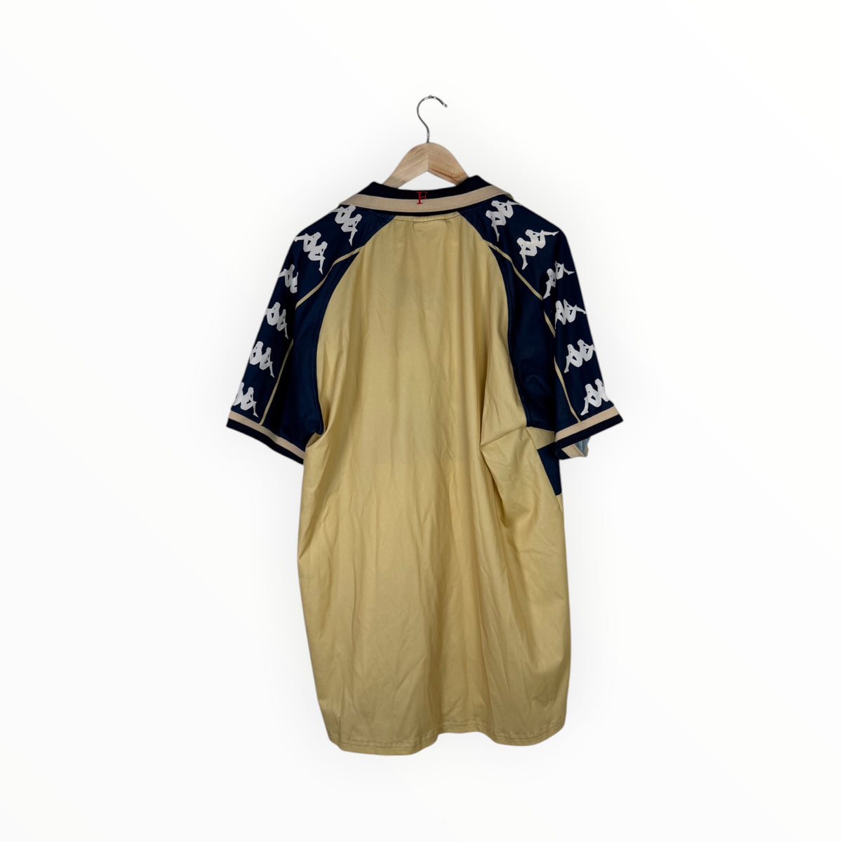 A vintage Kappa short-sleeve baseball-style shirt shown from the back, hanging on a wooden hanger against a plain white background. The shirt features a tan body with dark navy sleeves and white Kappa logos.