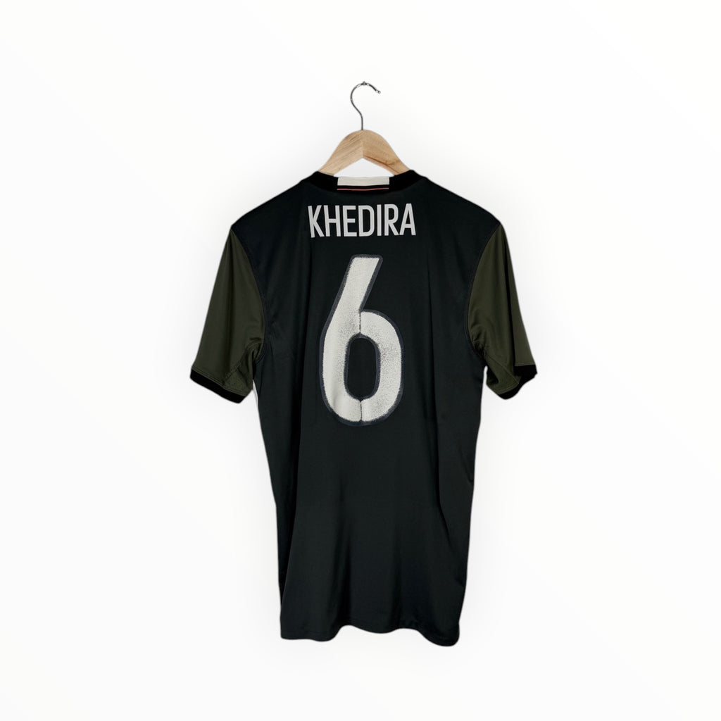 A black short-sleeve sports jersey with olive green side panels, hanging on a wooden hanger against a plain white background. The back of the shirt features the name 'KHEDIRA' and the number '6' in white.
