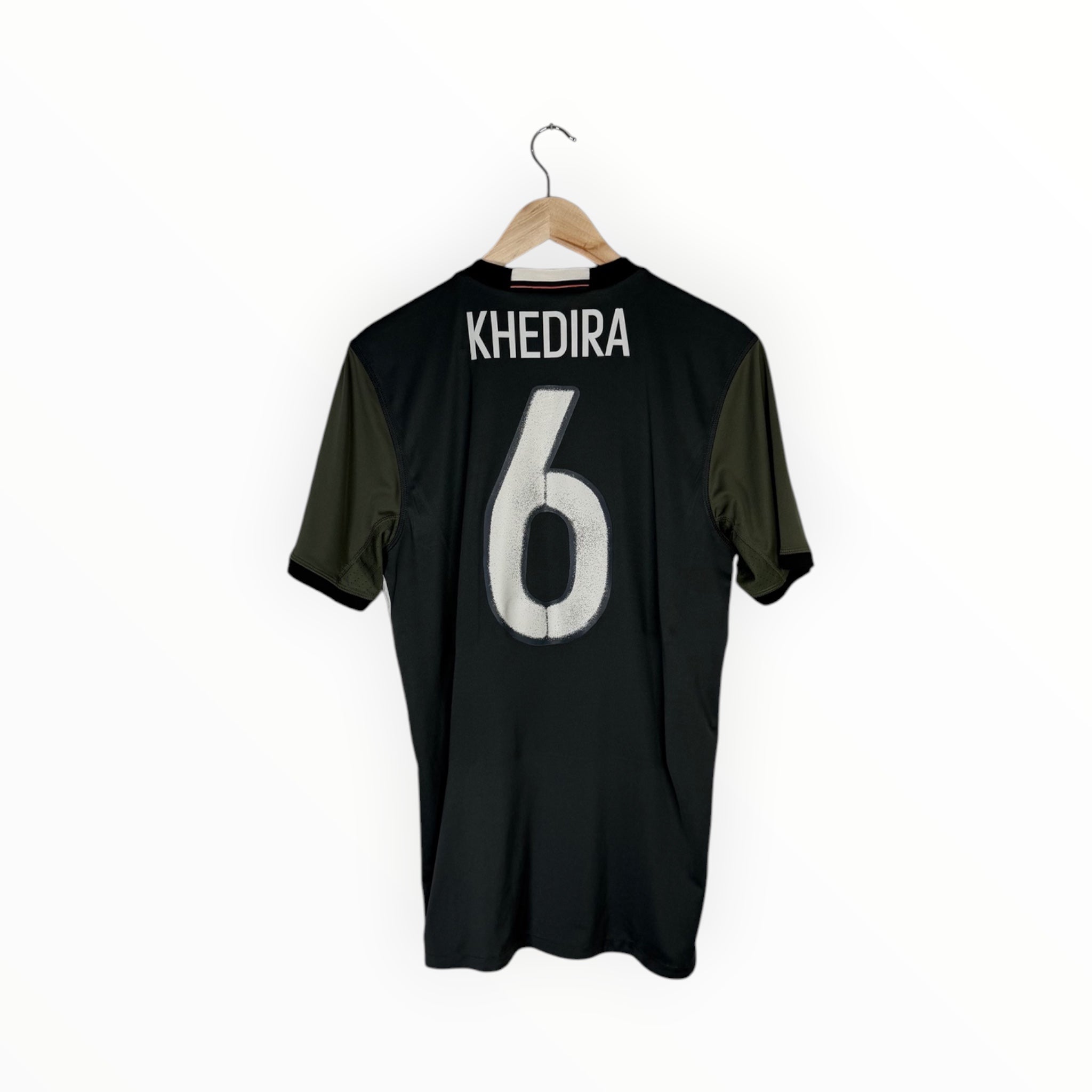 A black short-sleeve sports jersey with olive green side panels, hanging on a wooden hanger against a plain white background. The back of the shirt features the name 'KHEDIRA' and the number '6' in white.