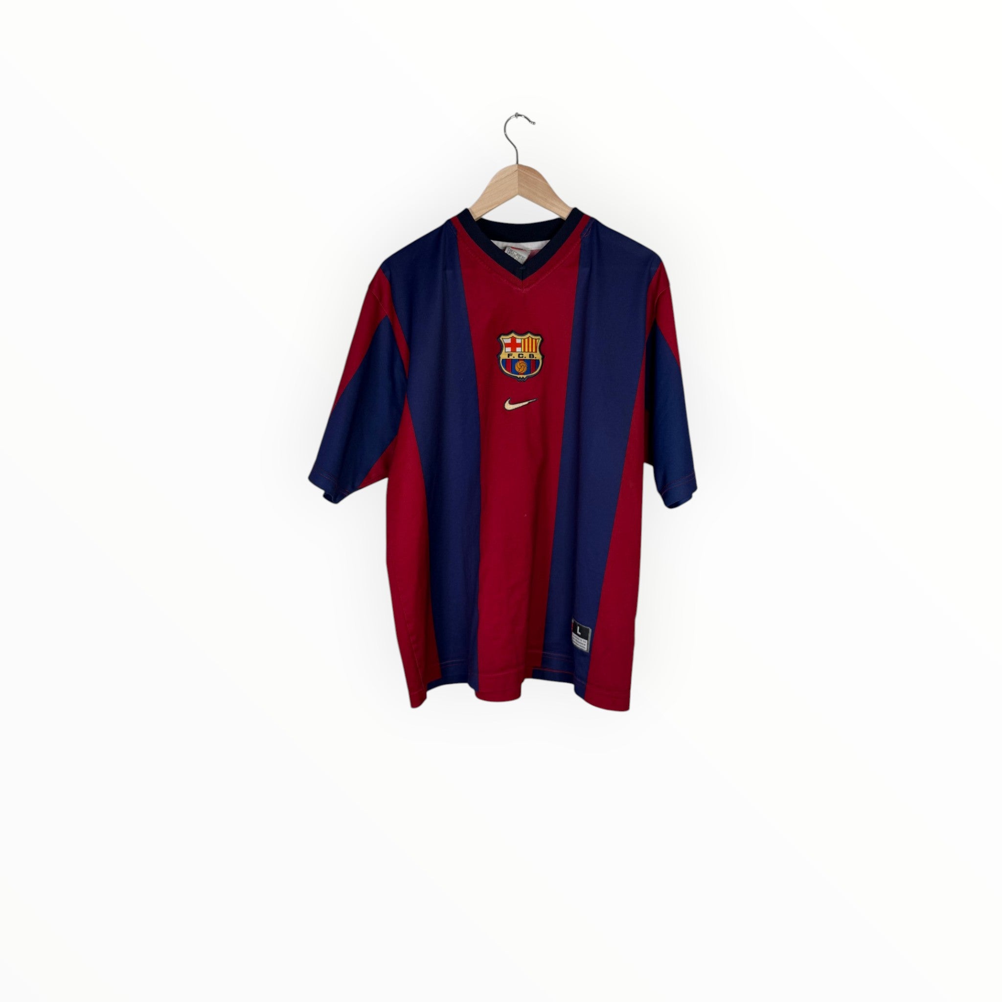 A vintage FC Barcelona home soccer jersey by Nike, featuring navy blue and red vertical stripes with the club crest on the chest, hanging on a wooden hanger against a plain white background.