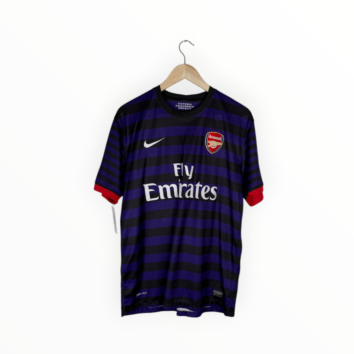 A Nike Arsenal home soccer jersey with dark purple and black horizontal stripes, featuring the Arsenal club crest on the left chest, a white Nike swoosh on the right chest, and 'Fly Emirates' sponsor text across the center. The jersey is shown hanging on a wooden hanger against a plain white background.