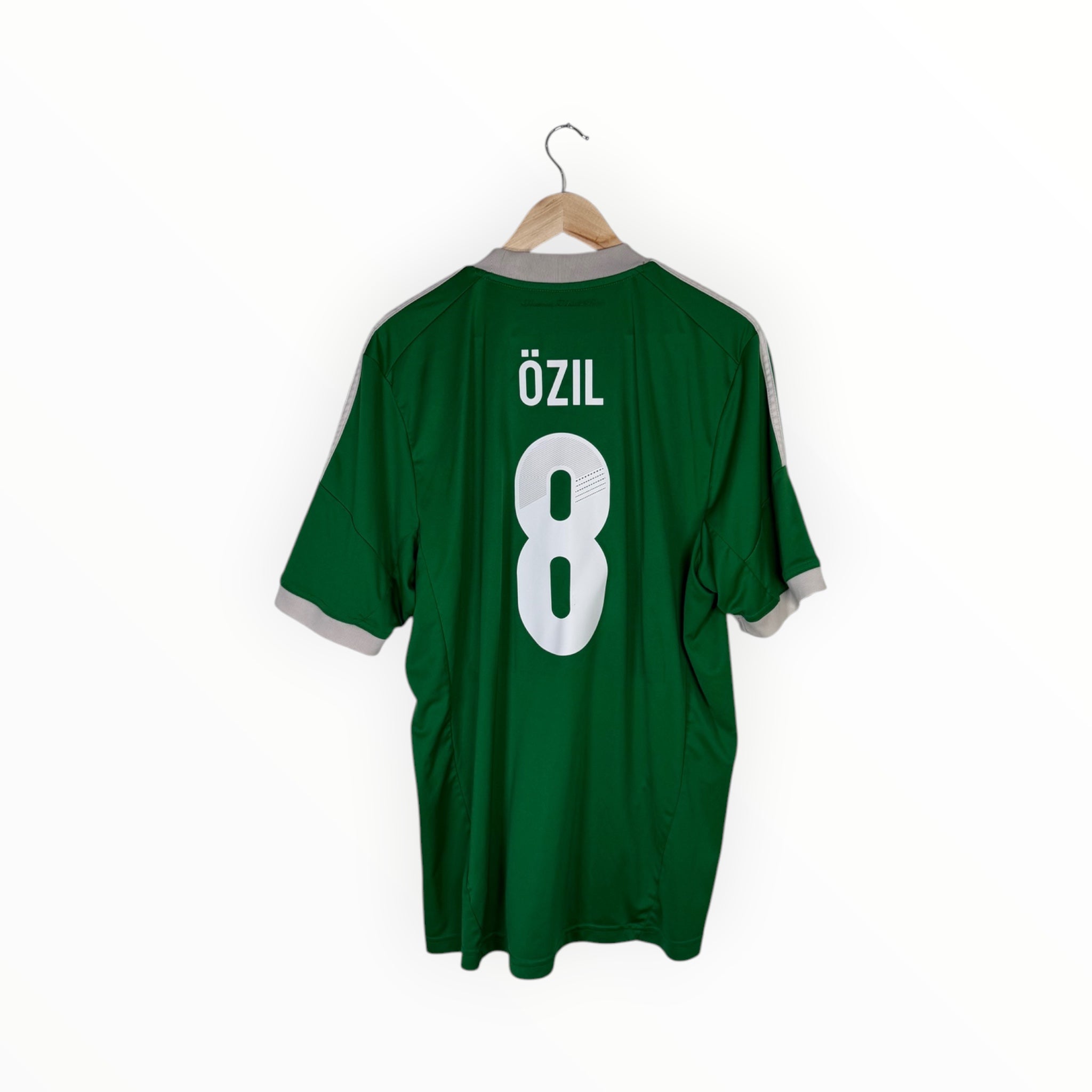 A green short-sleeve soccer jersey hanging on a wooden hanger against a white background, showing the back with the name 'ÖZIL' and number '8' in white.