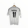 A white Real Madrid jersey with 'RODRYGO' and the number '11' printed in black on the back, hanging on a wooden hanger against a white background.