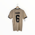 A beige soccer jersey with black trim, featuring the name 'POGBA' and number '6' on the back, hanging on a wooden hanger against a white background.