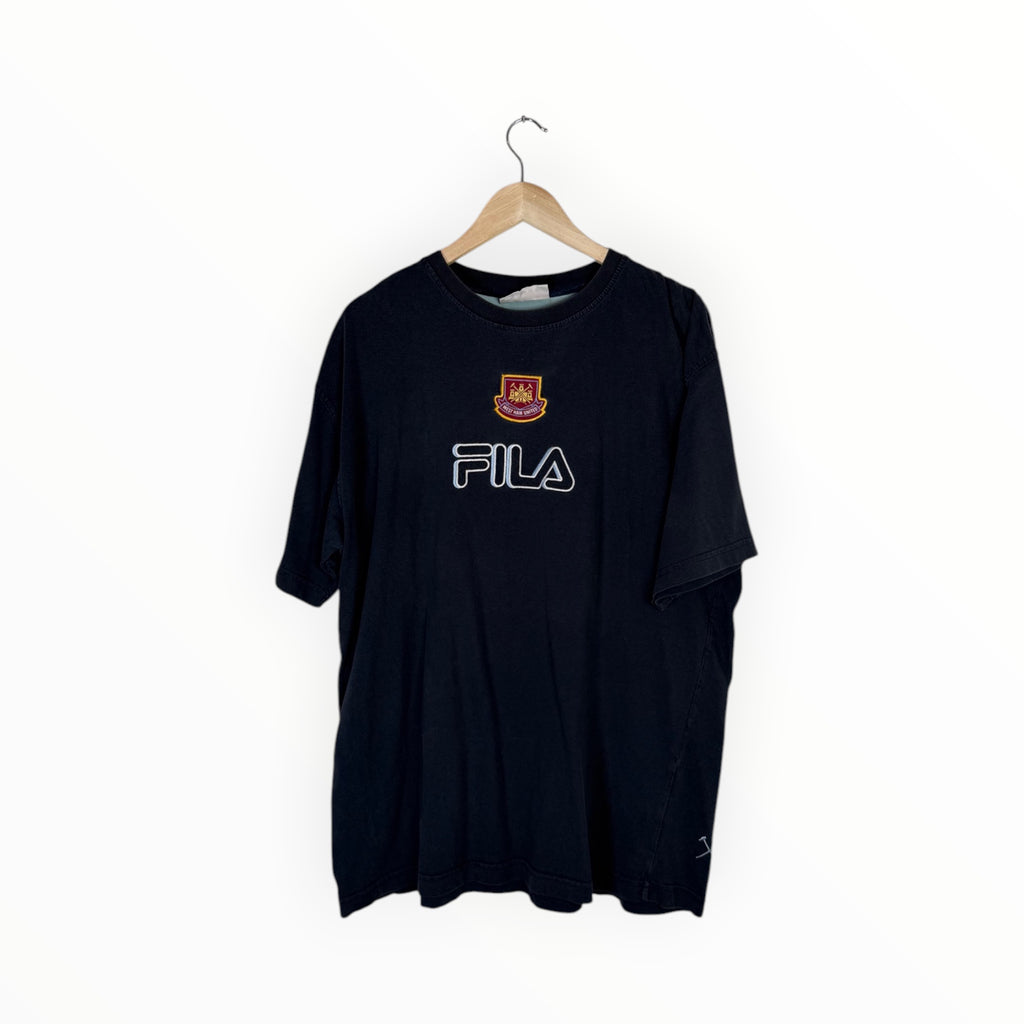 A black FILA t-shirt hanging on a wooden hanger against a plain white background. The shirt features the FILA logo in white outlined lettering across the chest and a small red and gold club crest above it.